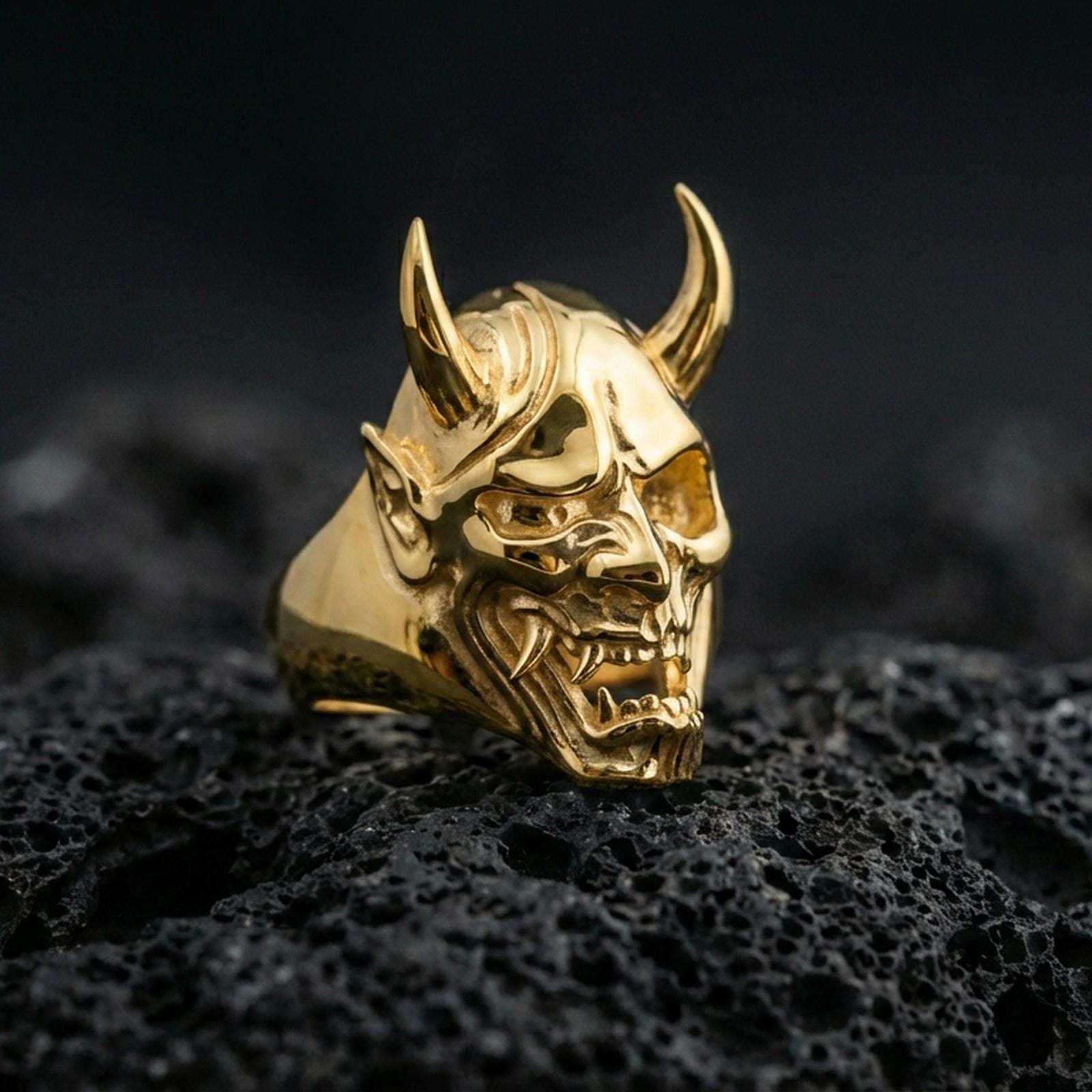 Sterling silver oni skull ring in polished silver finish on volcanic rock, detailed horned mask carving and fangs, close-up photo