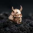 Load image into Gallery viewer, Oni mask skull ring in a rose gold plated finish on volcanic rock, ornate yokai demon face with horned profile, luxury studio close-up
