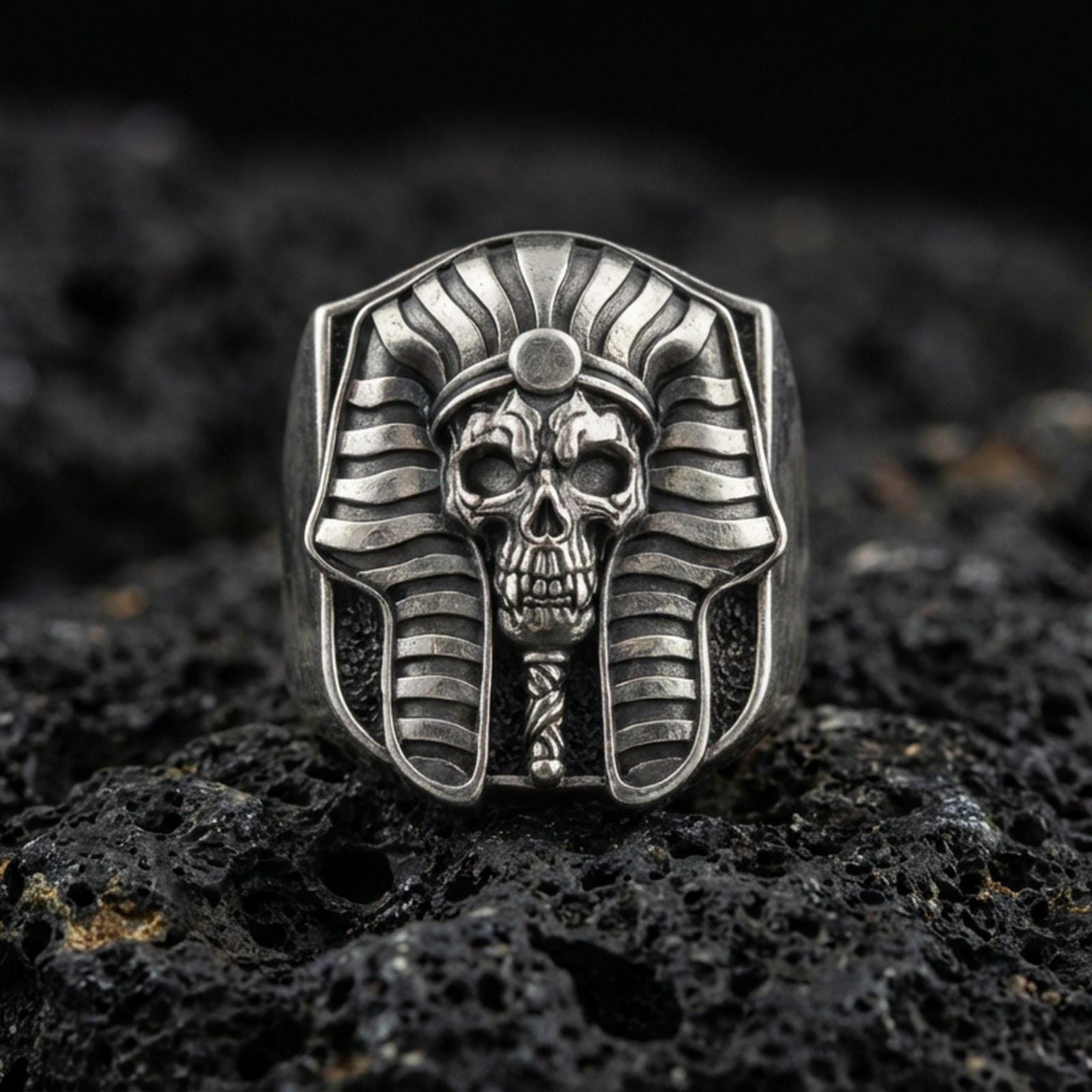 Sterling silver pharaoh skull ring in an oxidized finish on volcanic rock, ancient Egypt mummy mask design, macro studio product shot