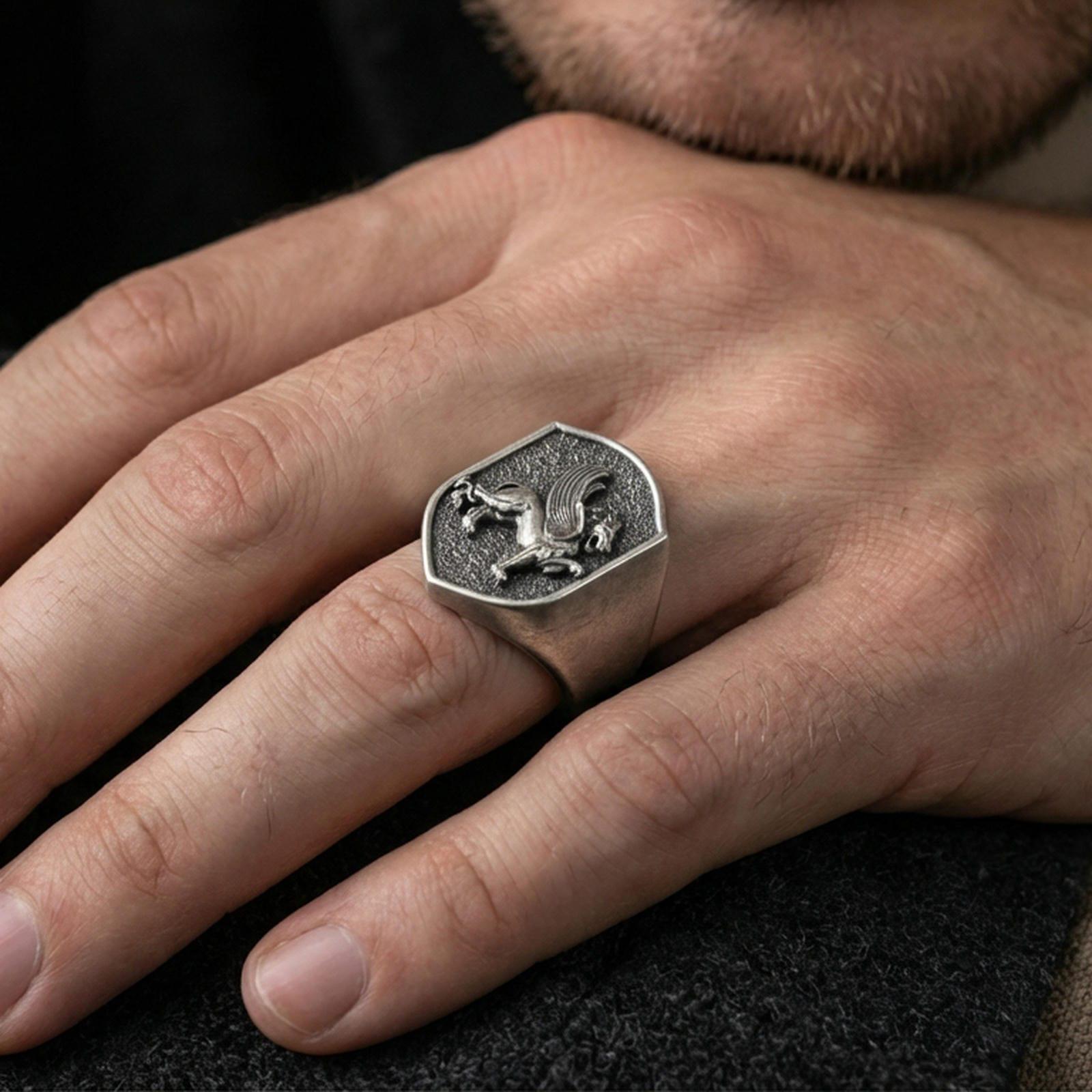 Sterling silver gryphon ring in an oxidized finish worn on finger, shield signet face with griffin relief visible, lifestyle hand close-up
