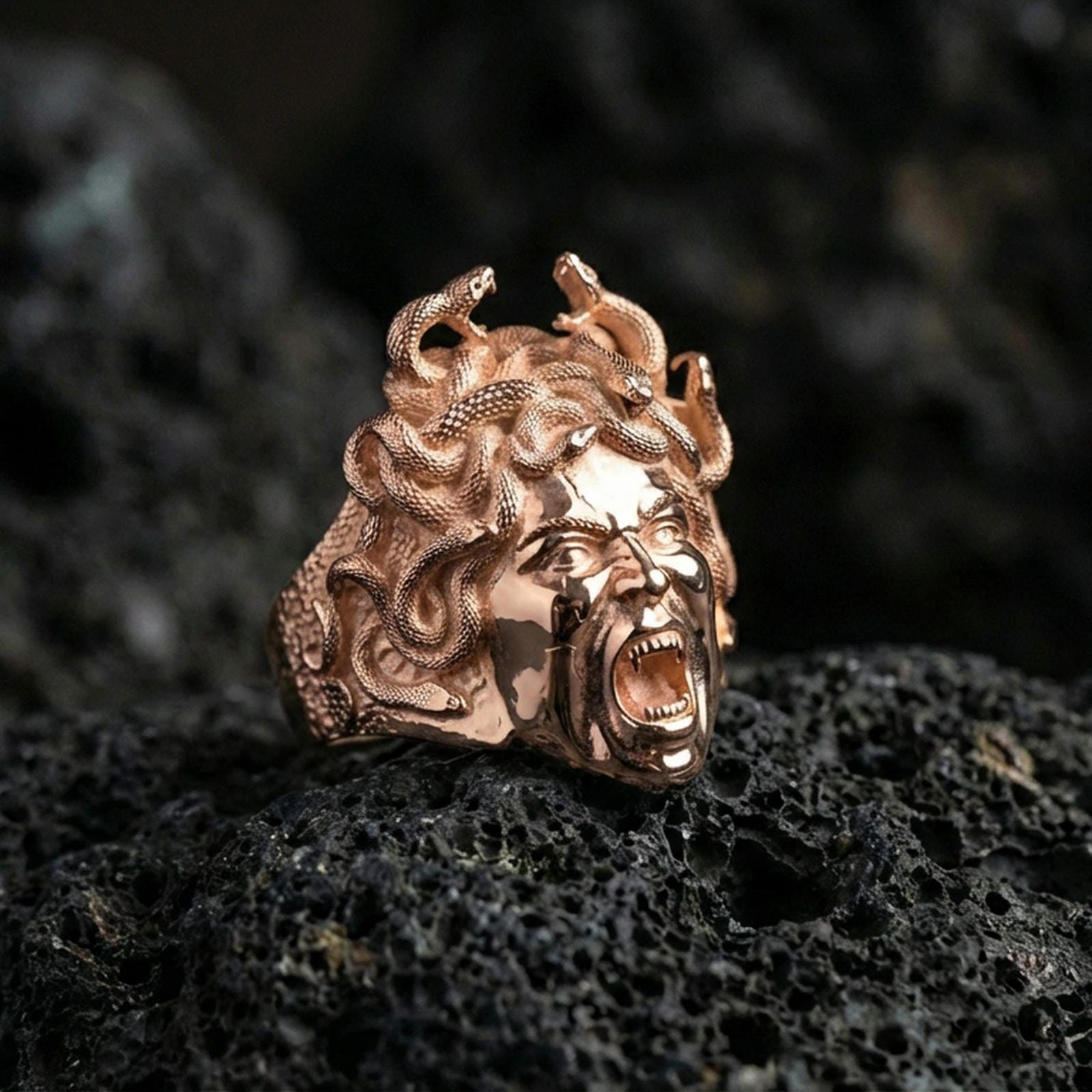 Medusa signet ring in a rose gold plated finish on volcanic rock, ornate gorgon snake hair sculpture, luxury studio close-up