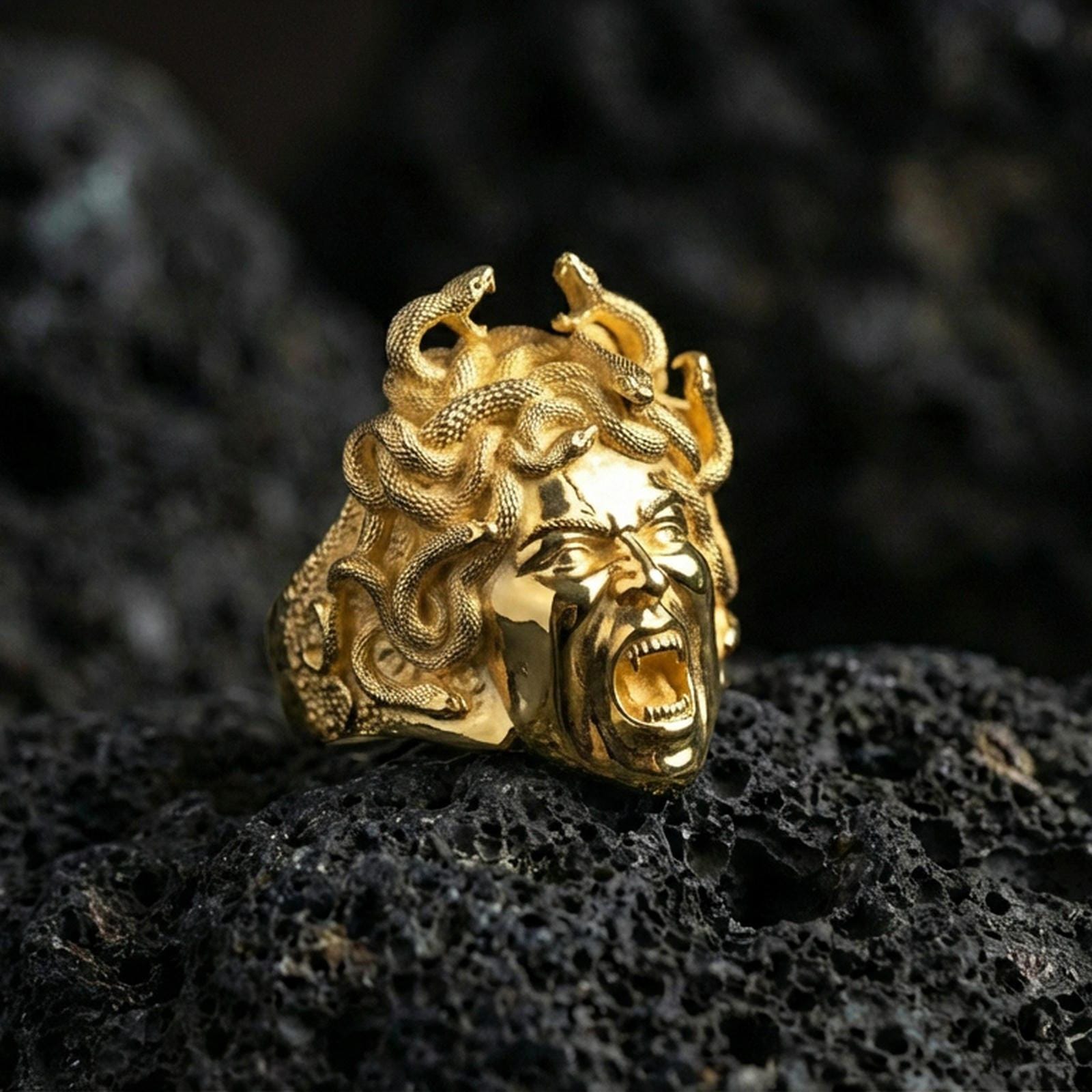 Medusa gorgon signet ring in a gold plated finish on volcanic rock, bold snake goddess statement design, premium macro product image