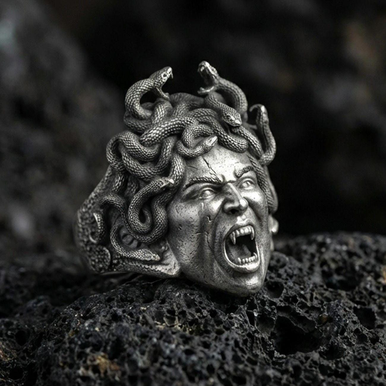 Sterling silver Medusa signet ring in an oxidized finish on volcanic rock, gorgon snake hair head sculpture with open mouth detail, macro studio product shot
