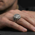 Load image into Gallery viewer, Sterling silver Yggdrasil ring in an oxidized finish worn on finger, tree of life emblem and side scrollwork visible, lifestyle hand close-up
