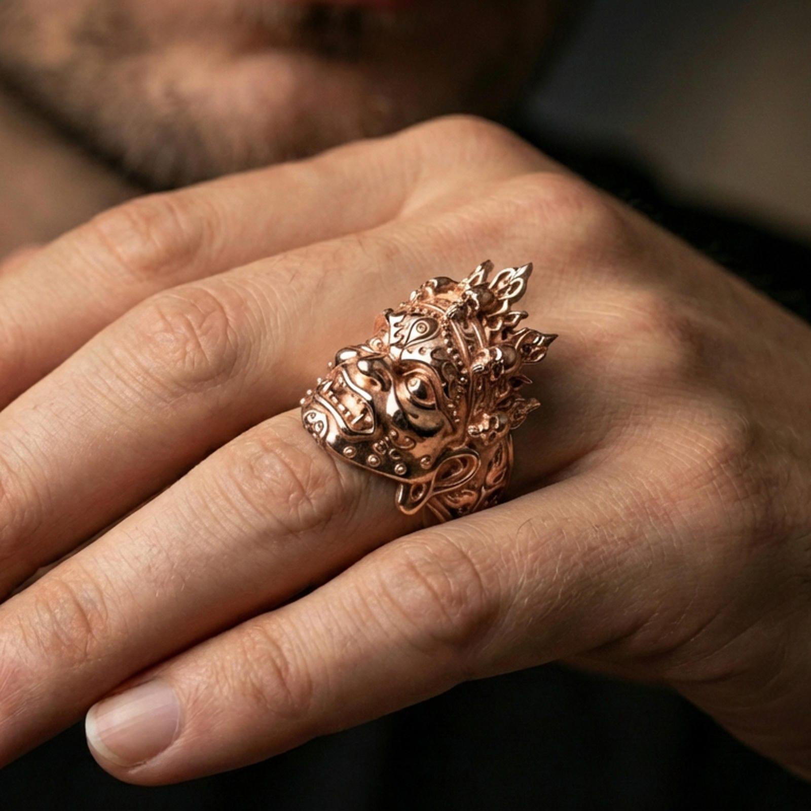 Yama mask ring in a rose gold plated finish on finger, ornate deity face relief and crown skull detailing, lifestyle hand close-up
