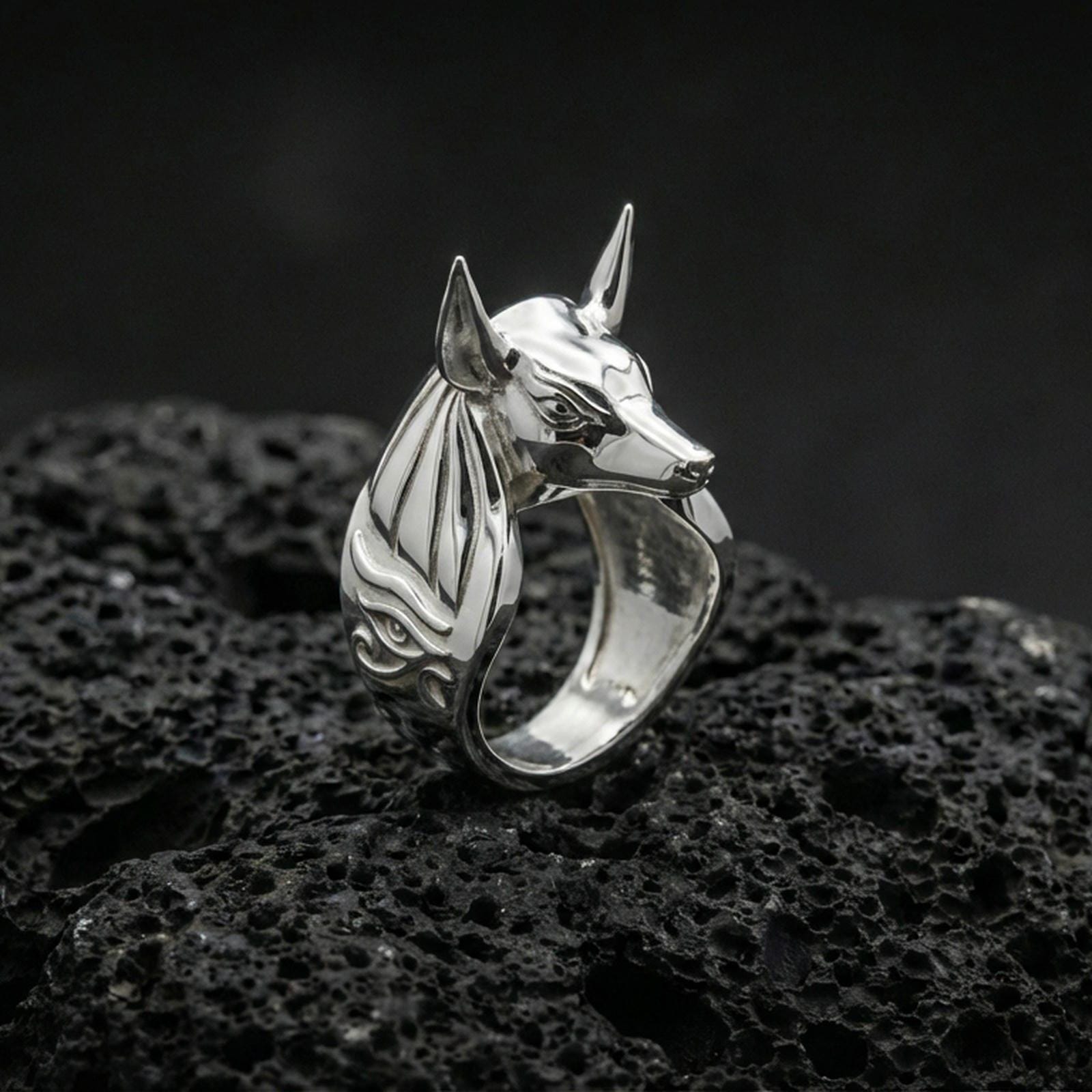 Anubis signet ring in polished silver finish on volcanic rock, sculpted jackal profile and smooth inner band, premium studio close-up