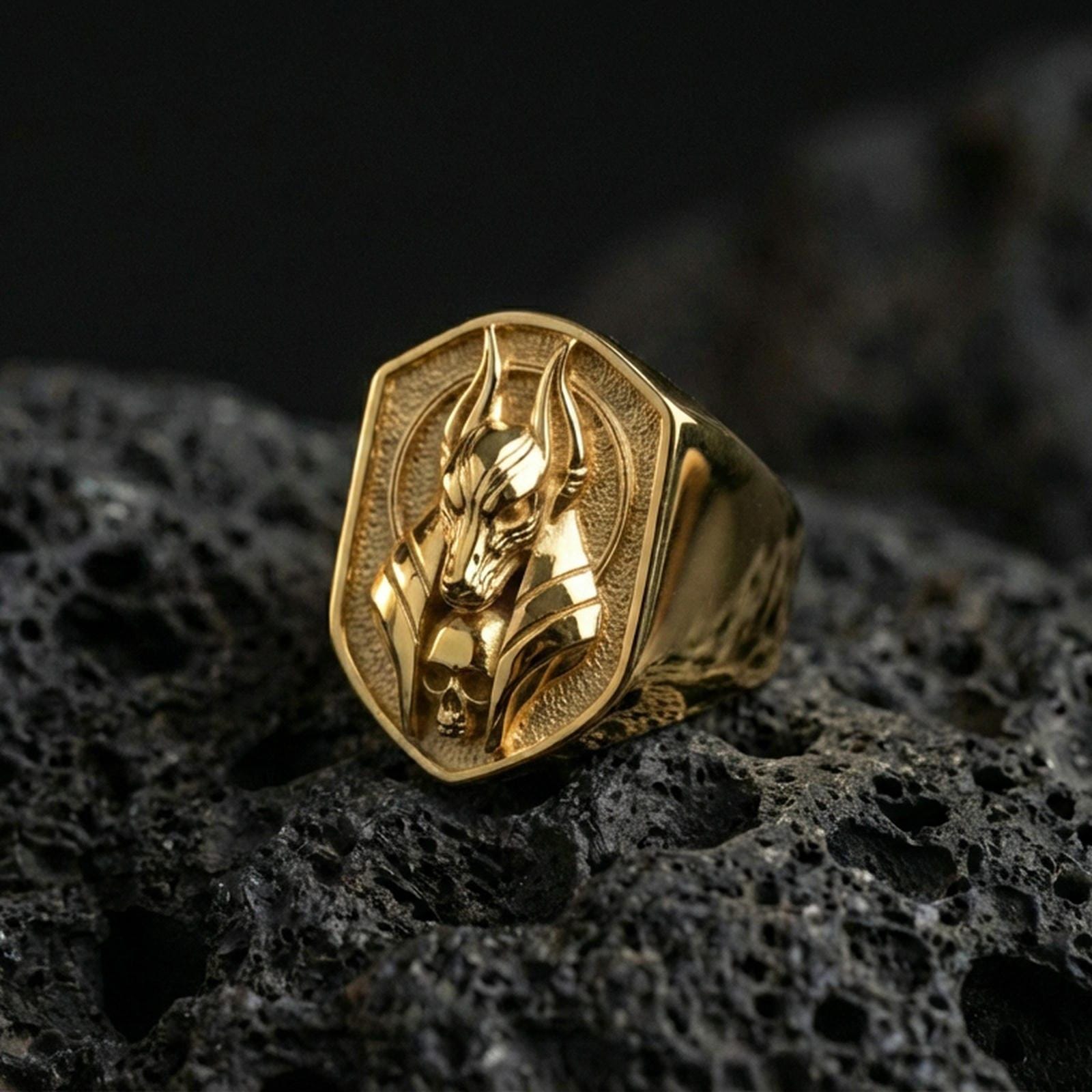 Egyptian Anubis ring in a gold plated finish on volcanic rock, protective jackal deity design with skull detail, luxury macro jewelry photo