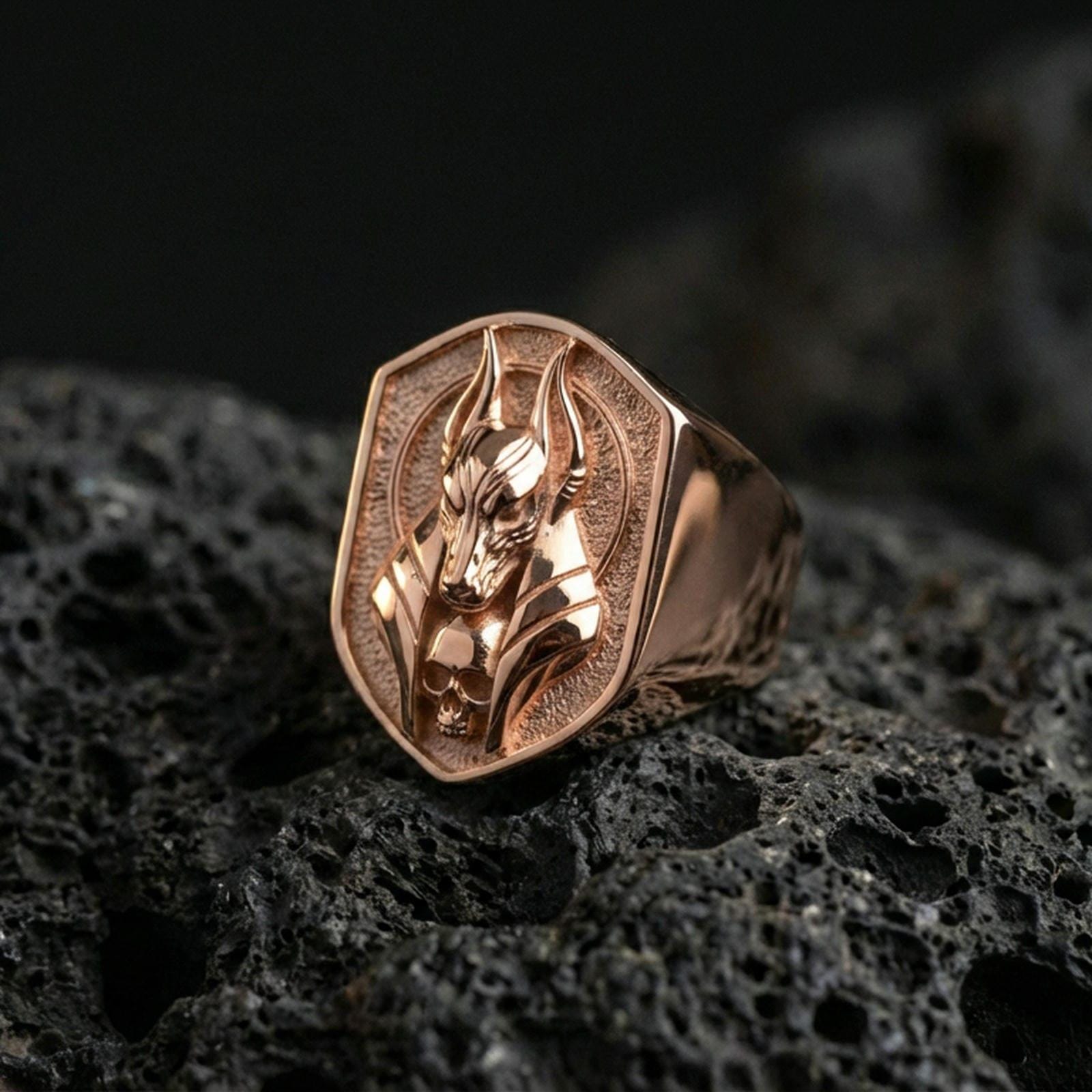 Anubis jackal head ring in a rose gold plated finish on volcanic rock, bold Egyptian protection symbol with sculpted faceplate, high-end close-up