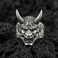 Load image into Gallery viewer, Sterling silver oni mask ring in an oxidized finish on volcanic rock, Japanese yokai demon face with sharp horns, detailed macro studio shot
