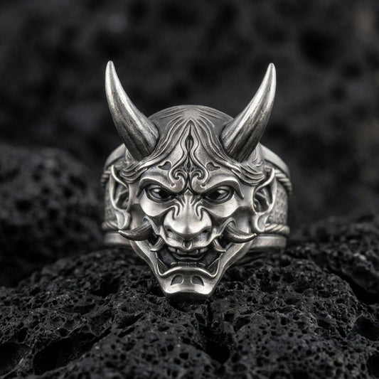 Sterling silver oni mask ring in an oxidized finish on volcanic rock, Japanese yokai demon face with sharp horns, detailed macro studio shot