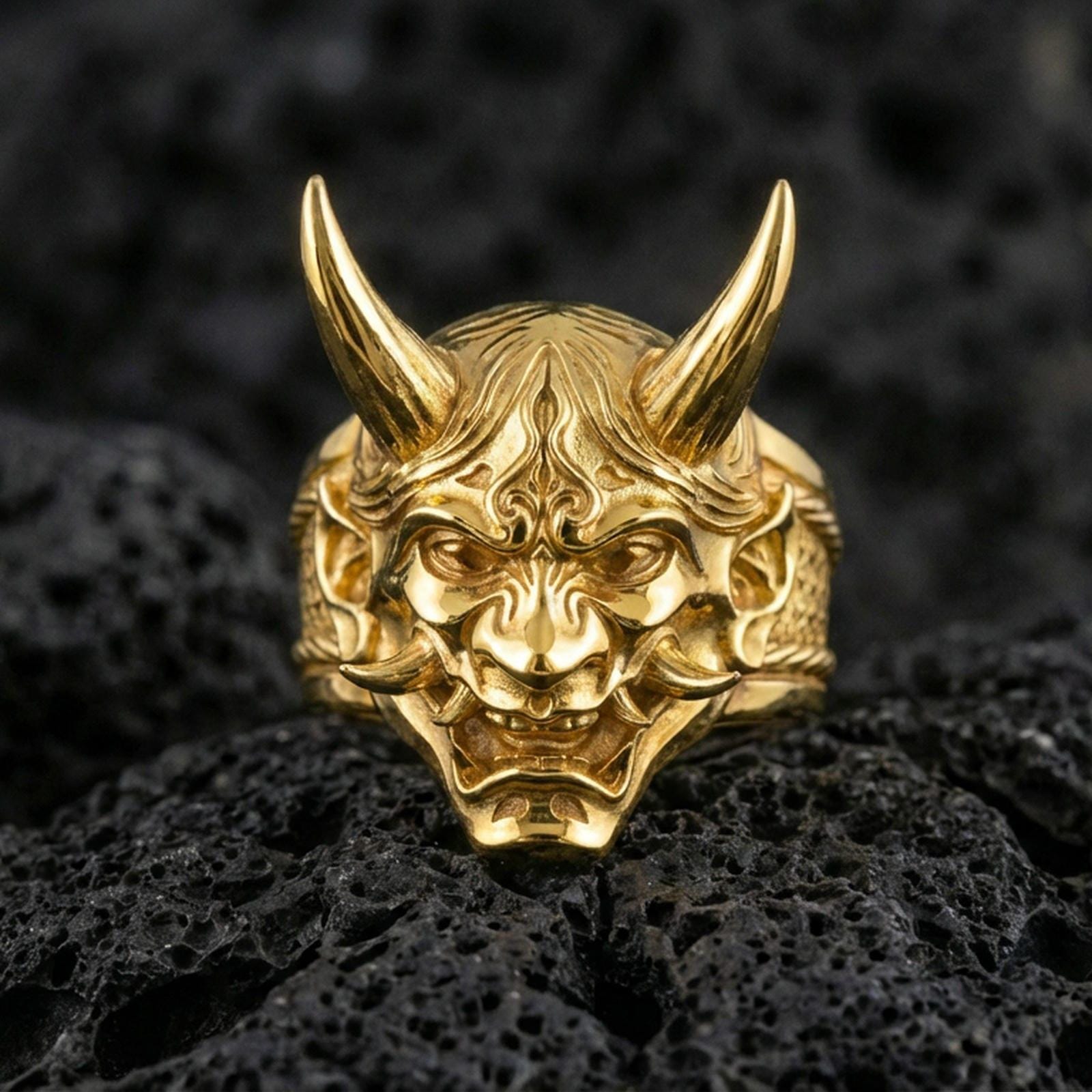 Japanese oni mask ring in a gold plated finish on volcanic rock, horned demon relief with fierce expression, luxury macro product image