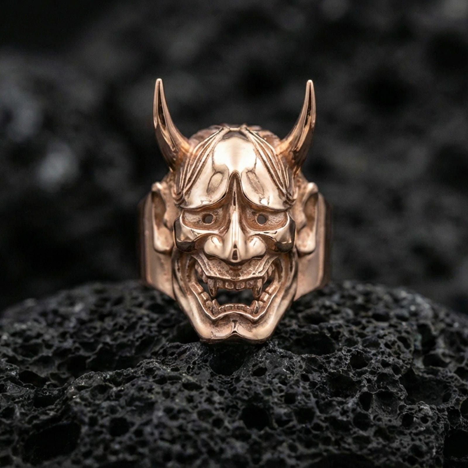 Sterling silver Hannya ring in a rose gold plated finish on volcanic rock, fierce demon mask relief with textured face details, close-up