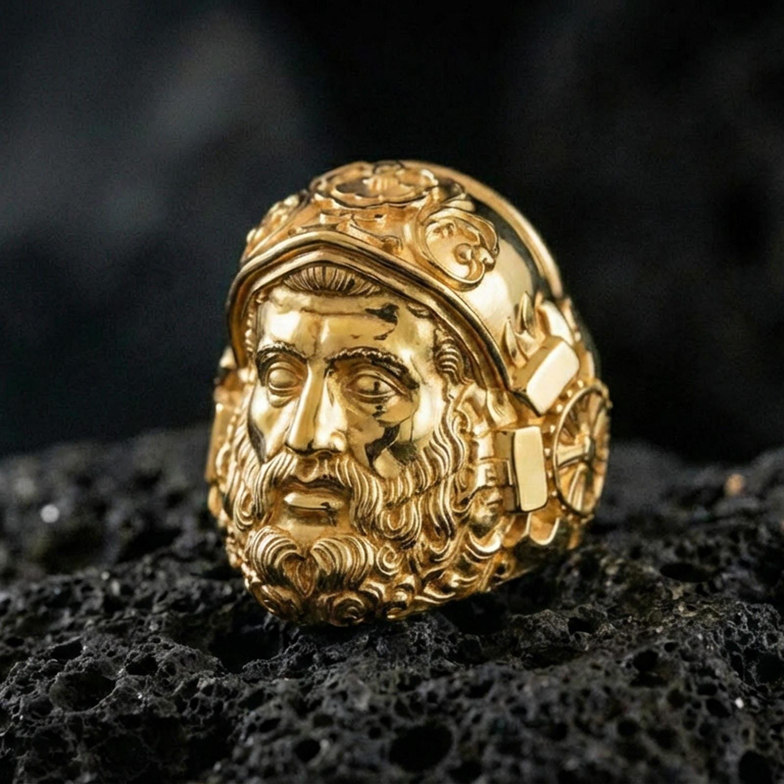 Gold plated Hephaestus signet ring on volcanic rock, bold blacksmith god portrait ring with strong artisan aesthetic
