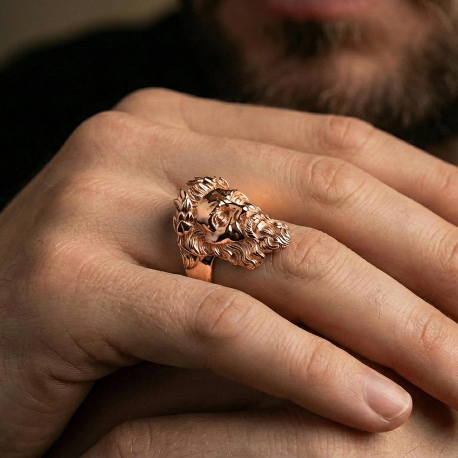 Rose gold plated Zeus ring on finger featuring ornate laurel wreath and sculpted face, refined lifestyle jewelry wear shot