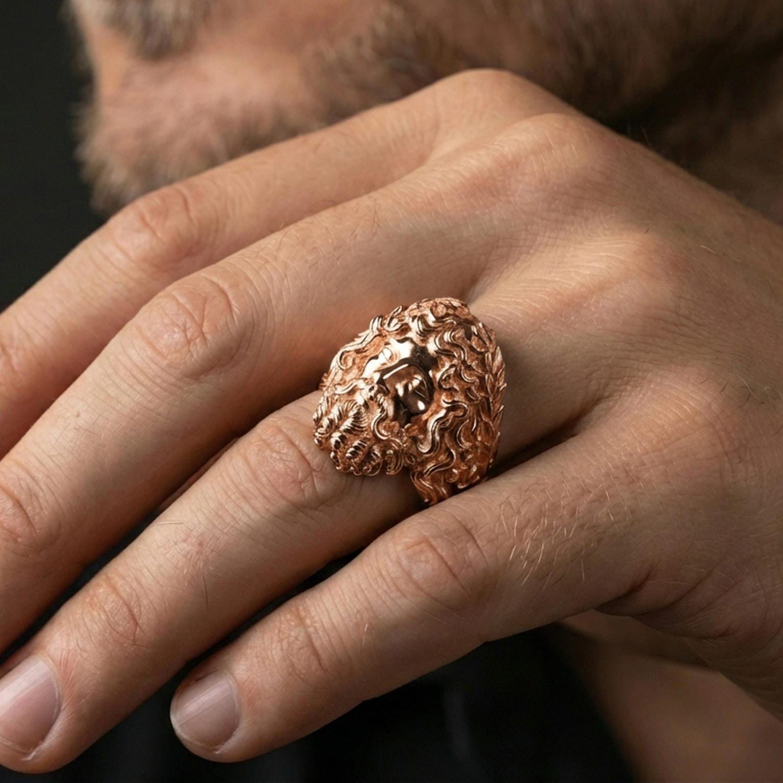 Rose gold plated Zeus head ring on finger, ornate Greek god face design, refined lifestyle jewelry wear shot