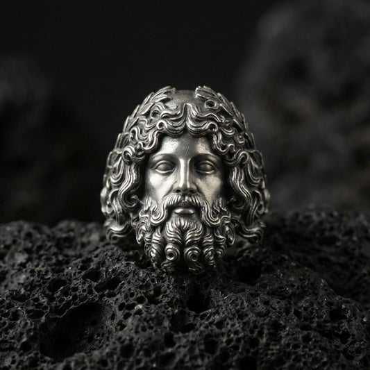 Detailed Zeus head ring crafted in oxidized sterling silver, expressive Greek god facial features, macro product shot on textured volcanic rock background