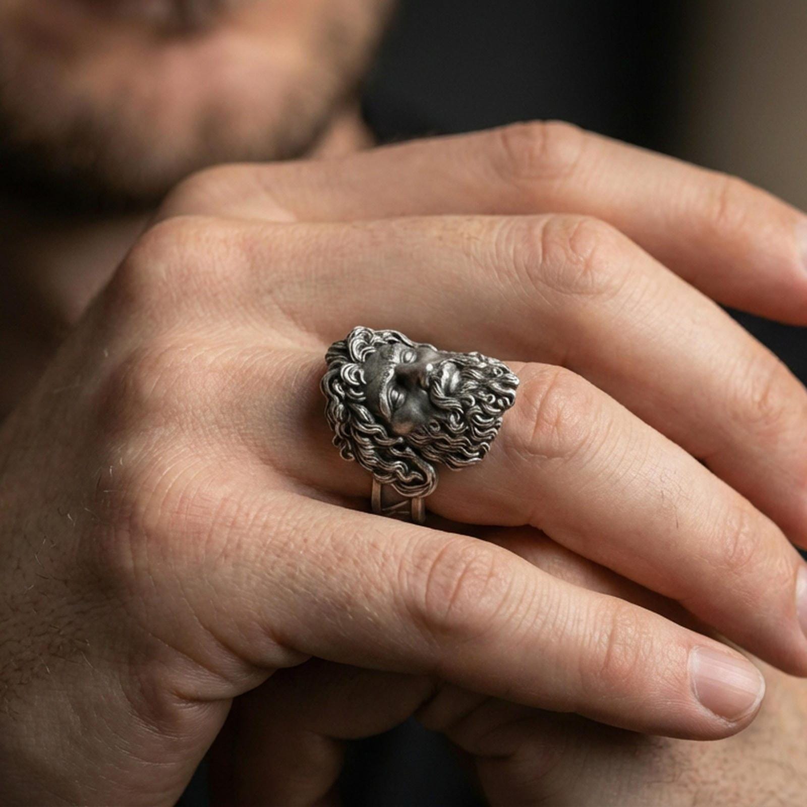 Oxidized sterling silver Zeus ring worn on finger, bold Greek mythology signet with powerful facial features, masculine lifestyle hand shot