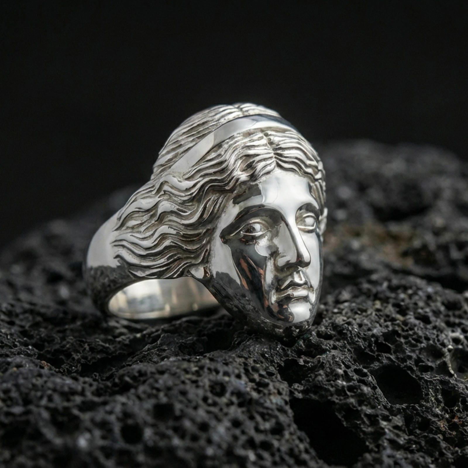 Polished silver Venus de Milo ring featuring serene goddess facial expression and flowing hair details, centered close-up on dark porous volcanic stone