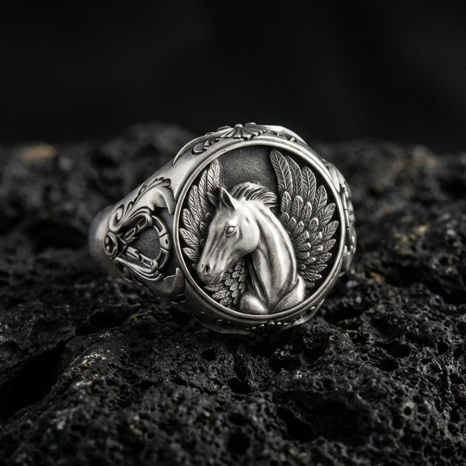 Detailed Pegasus ring crafted in oxidized sterling silver, winged mythical horse relief, macro product shot on textured volcanic rock background