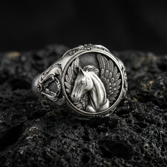 Detailed Pegasus ring crafted in oxidized sterling silver, winged mythical horse relief, macro product shot on textured volcanic rock background