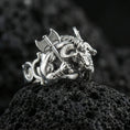 Load image into Gallery viewer, Polished silver Minotaur ring featuring powerful mythological creature with horns and battle axe, centered close-up on dark porous volcanic stone

