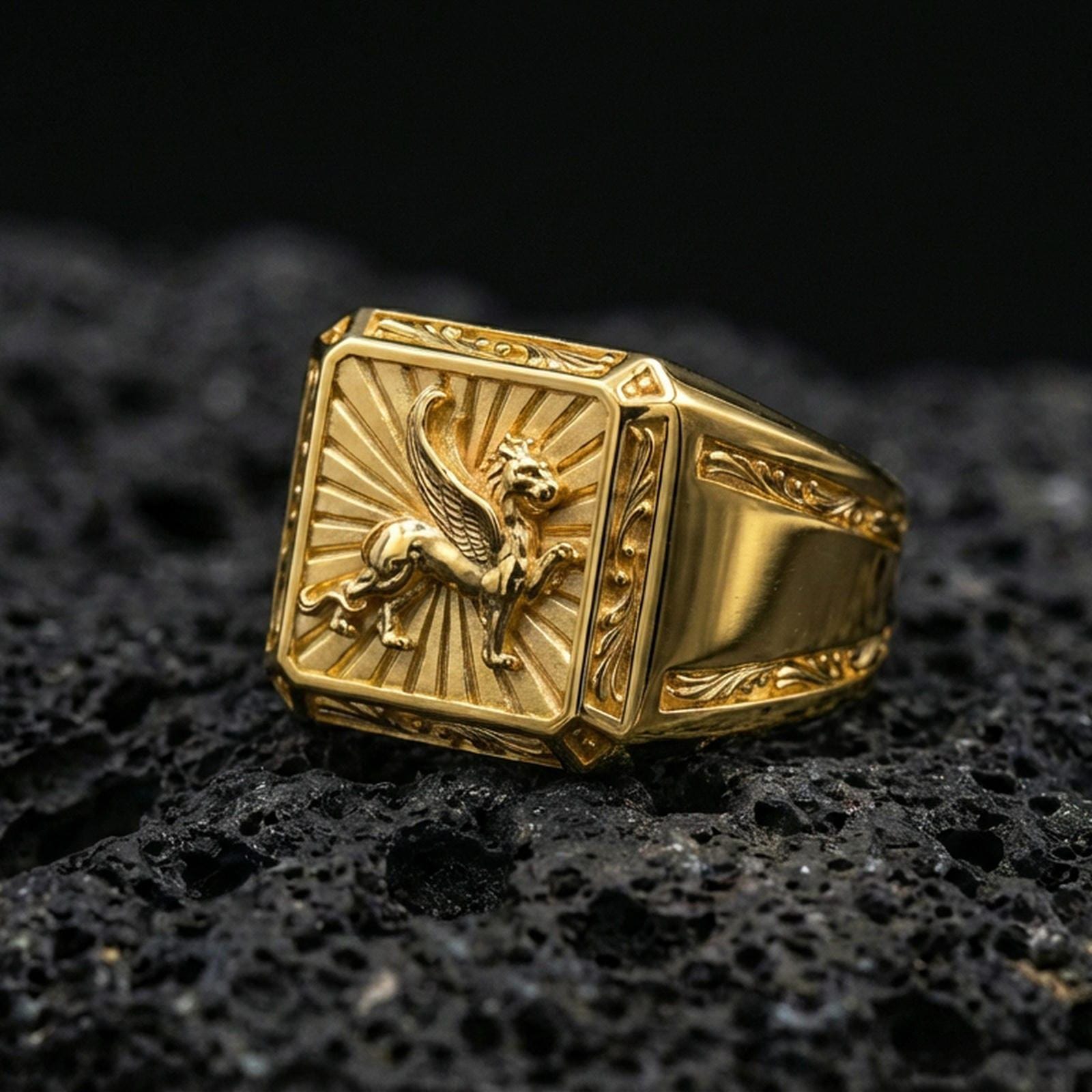 Gold plated gryphon signet ring with high-relief winged creature motif and ornate engraved sides, premium studio macro on black volcanic rock surface