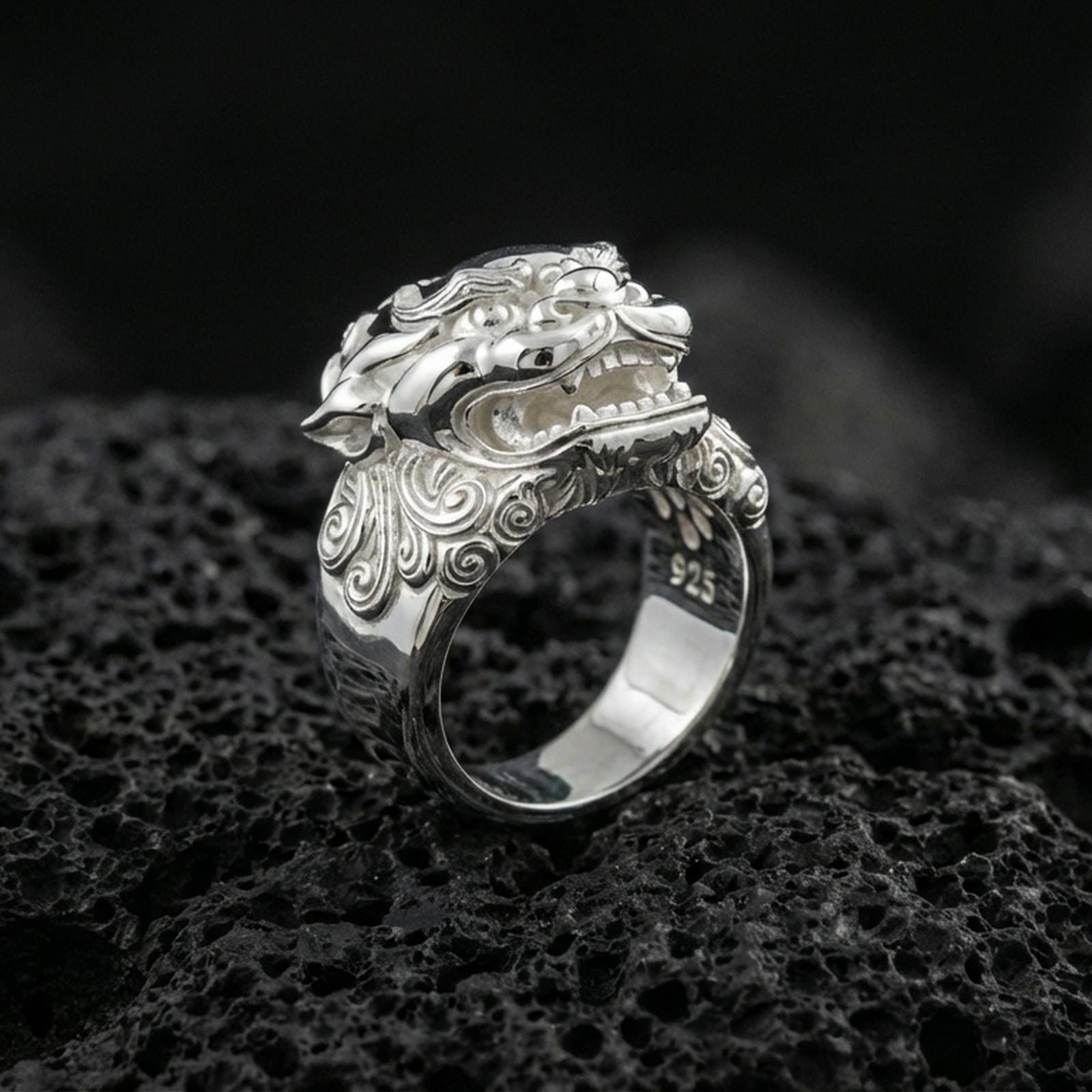 Polished silver Foo Dog ring featuring sculpted guardian lion face and flowing scrollwork details, centered close-up on dark porous volcanic stone