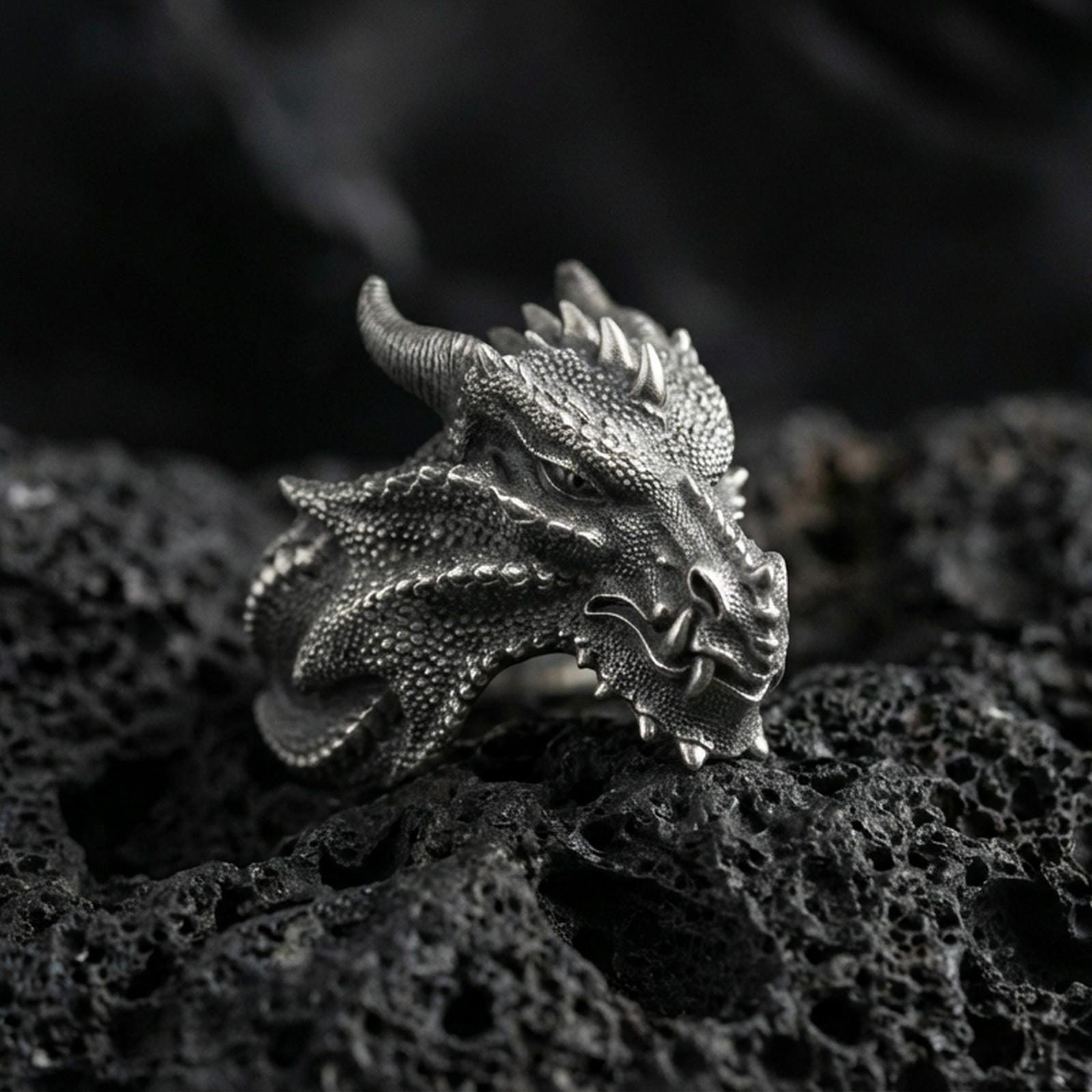 Detailed dragon wyrm ring crafted in oxidized sterling silver, textured scale pattern with horned dragon head, macro product shot on textured volcanic rock background