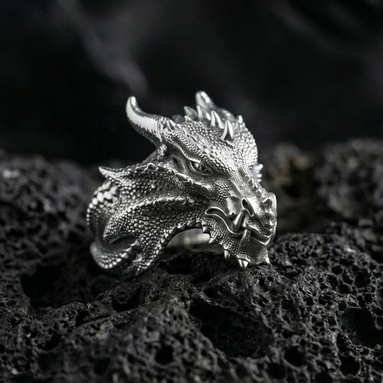 Polished silver dragon ring featuring sculpted horns and intricate reptile scale texture, centered close-up jewelry photo on dark porous volcanic stone