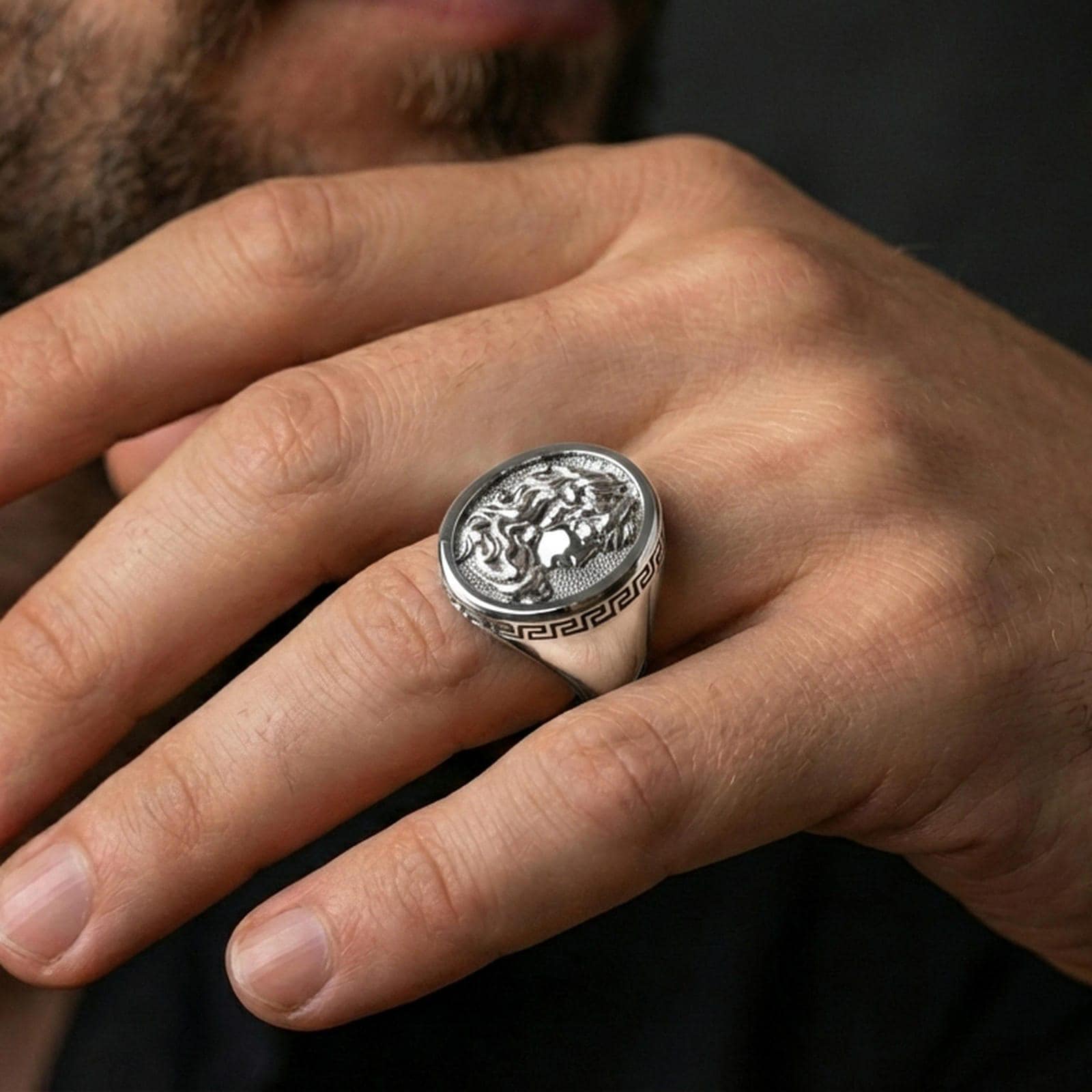 Polished silver Medusa signet ring on finger highlighting serpent hair details and classic Greek pattern band, clean lifestyle wear photo