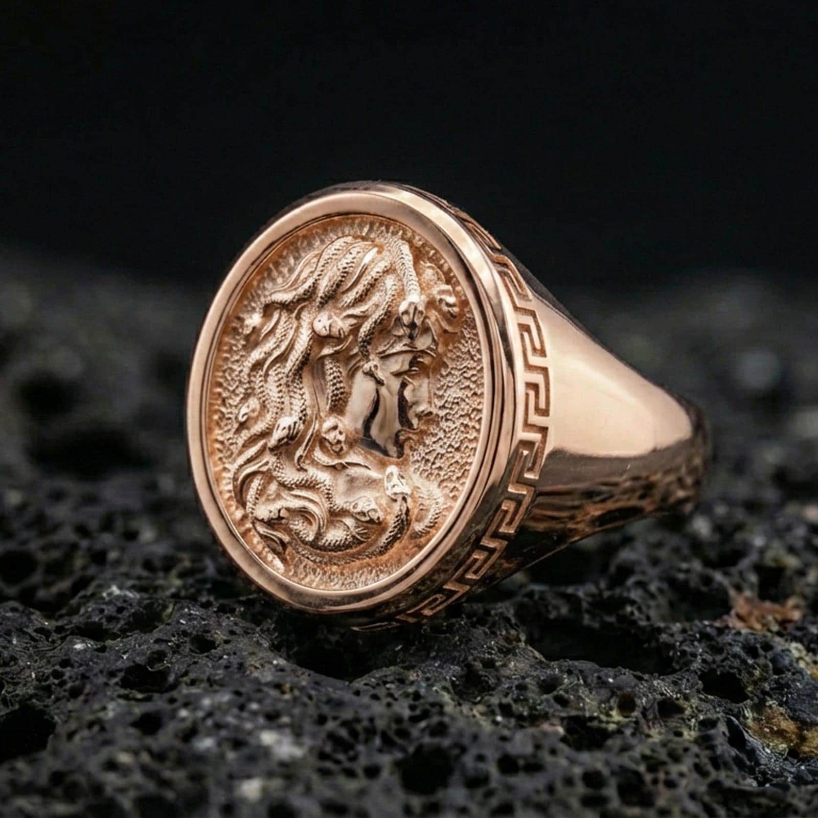 Rose gold plated Medusa ring showcasing detailed ancient Greek Medusa profile and textured background, sharp close-up product photography on volcanic rock