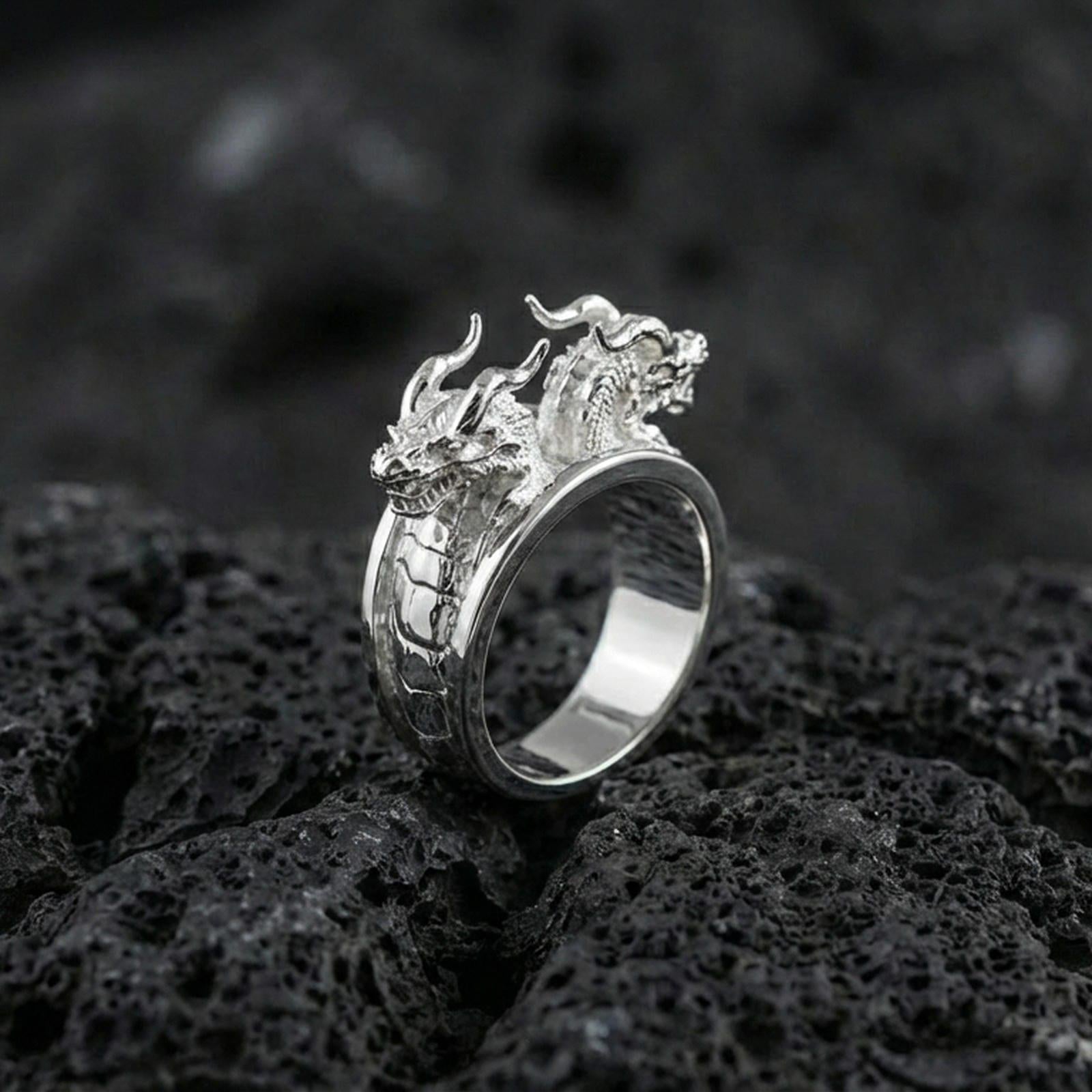Polished silver twin dragons ring featuring paired dragon head design and engraved scale detailing, centered close-up on dark porous volcanic stone