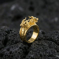 Load image into Gallery viewer, Gold plated twin dragons ring with high-relief dragon heads and textured scales on an open wrap band, premium studio macro on black volcanic rock surface
