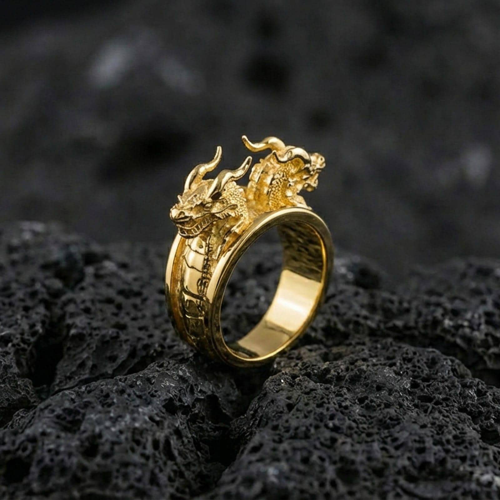 Gold plated twin dragons ring with high-relief dragon heads and textured scales on an open wrap band, premium studio macro on black volcanic rock surface