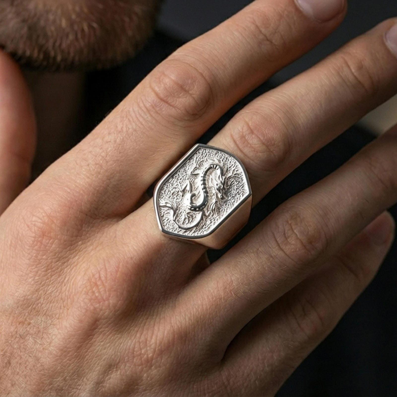 Polished silver Chinese dragon ring on finger highlighting shield-shaped signet and raised dragon relief, clean lifestyle wear photo