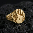 Load image into Gallery viewer, Gold plated handprint signet ring with gothic skull band and round textured face, premium studio close-up on volcanic rock background
