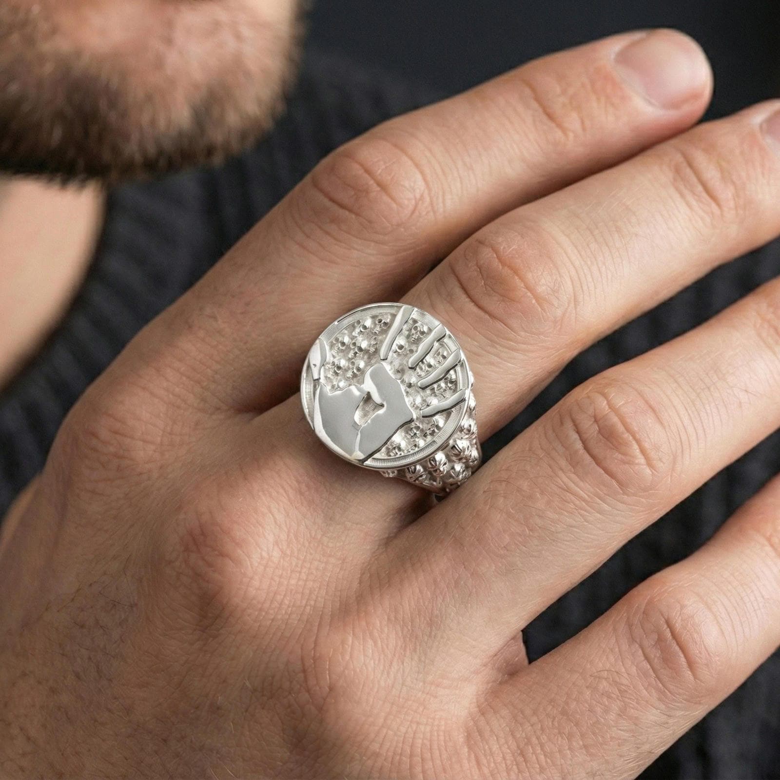 Polished silver assassin handprint ring on finger highlighting raised seal design and skull texture, everyday unisex style photo