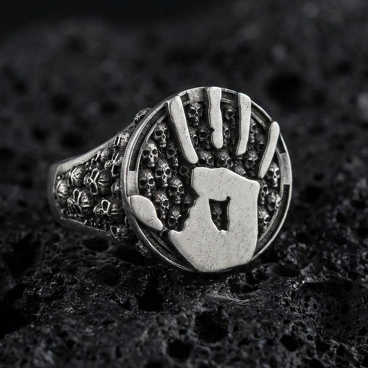 Oxidized sterling silver assassin handprint signet ring with skull band texture, dark fantasy statement jewelry on black volcanic rock