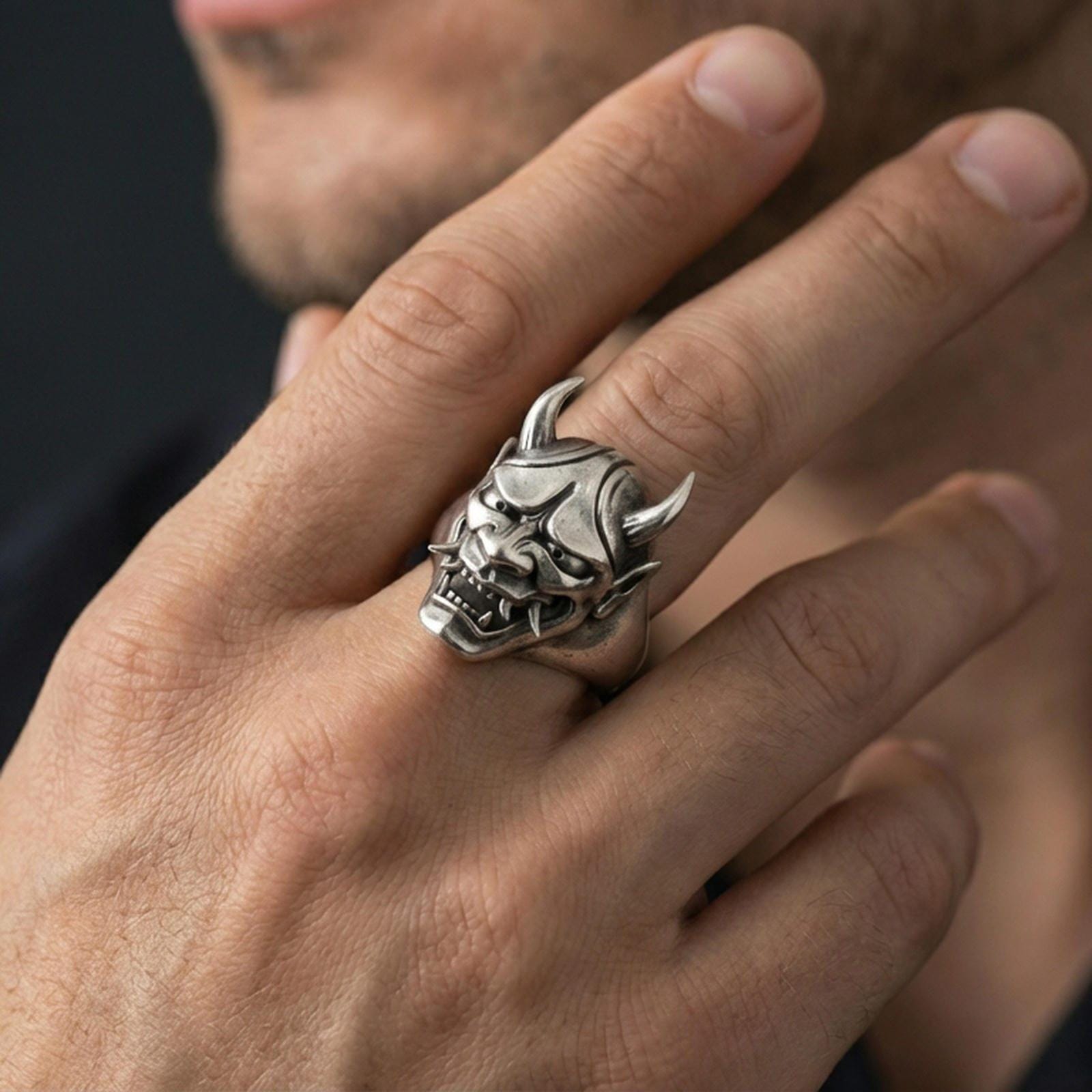 Oxidized sterling silver Oni mask ring on a human finger, Japanese demon signet with horns and fangs, dark gothic streetwear styling