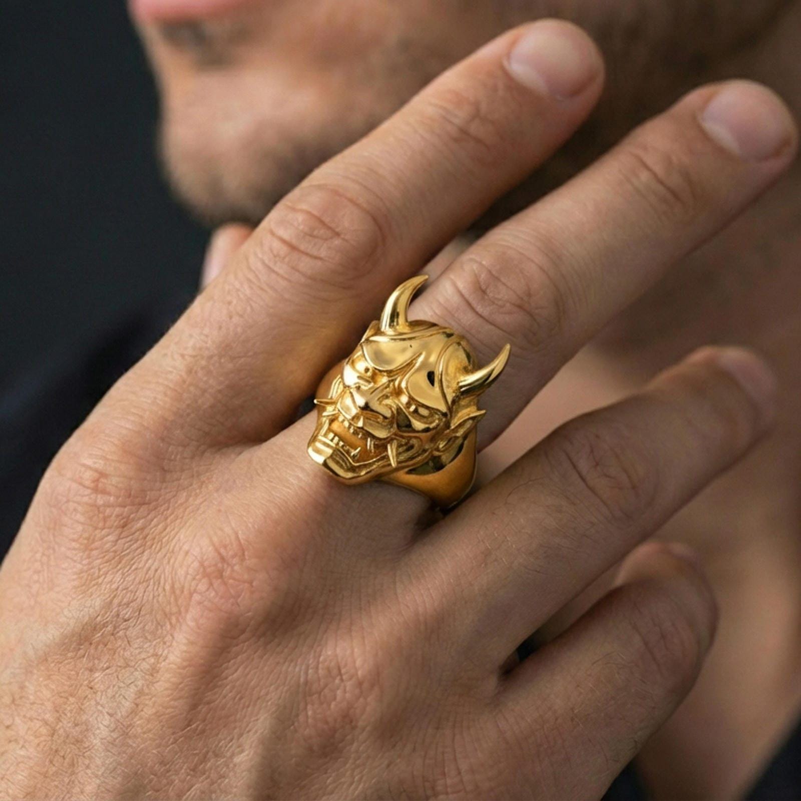 Gold plated Oni mask ring on a human finger, Japanese demon mask signet, horned fierce expression, bold fantasy jewelry