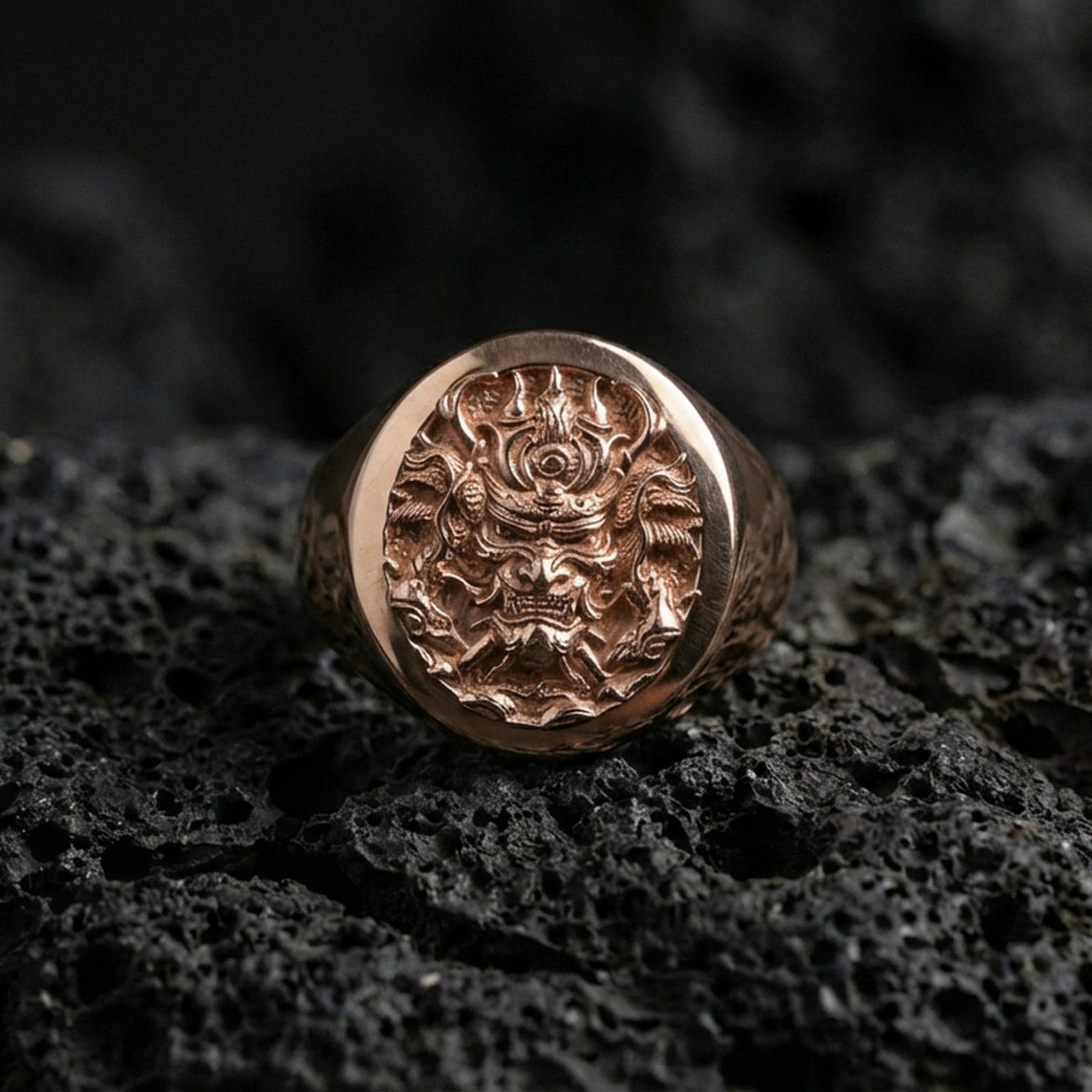 Rose gold plated samurai warrior signet ring on black volcanic stone, ornate samurai mask engraving, high-detail statement ring