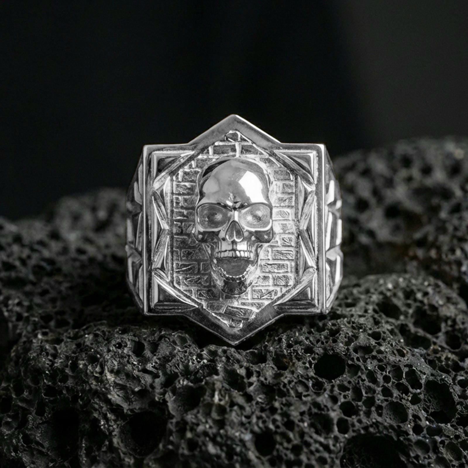 Polished sterling silver skull signet ring on black volcanic stone, raised skull face, brick wall engraving
