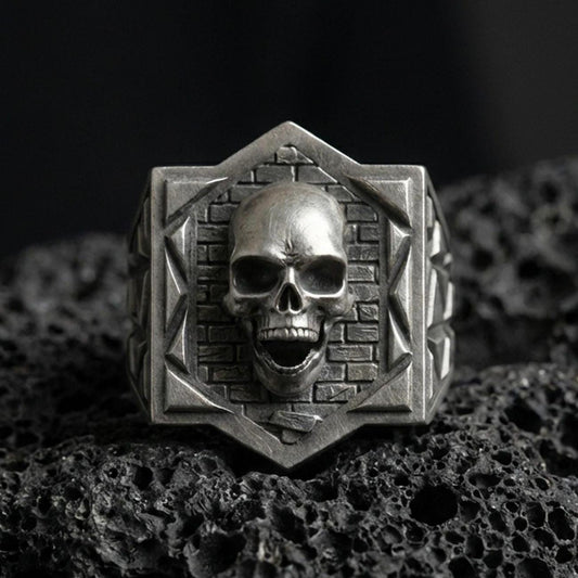 Oxidized sterling silver skull signet ring on black volcanic stone, brickwork background, gothic statement jewelry