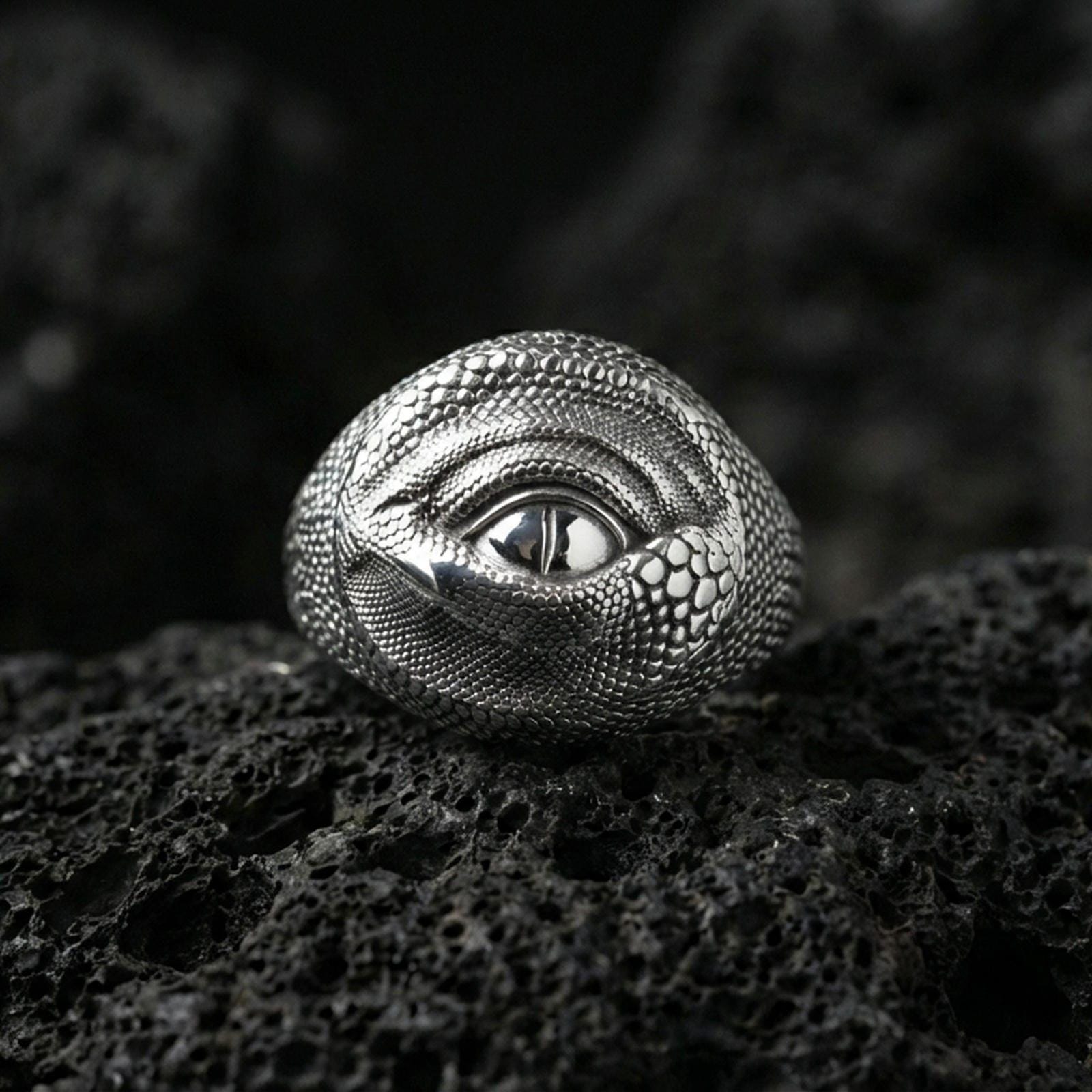 Polished sterling silver dragon eye ring on black volcanic stone, realistic scaled texture with central eye, fantasy statement ring