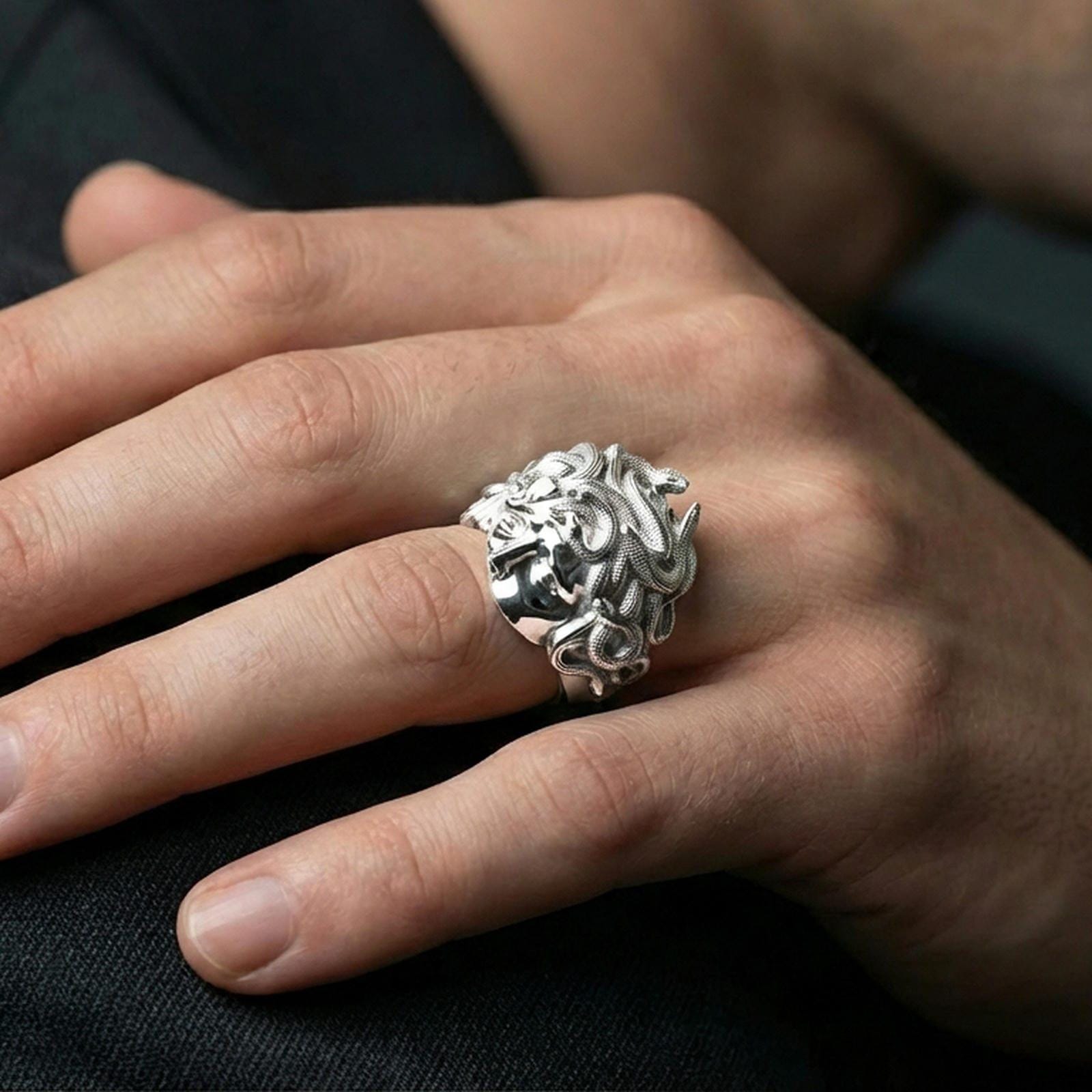 Polished sterling silver Medusa head ring on a human finger, detailed gorgon face and serpents, antique-inspired signet ring