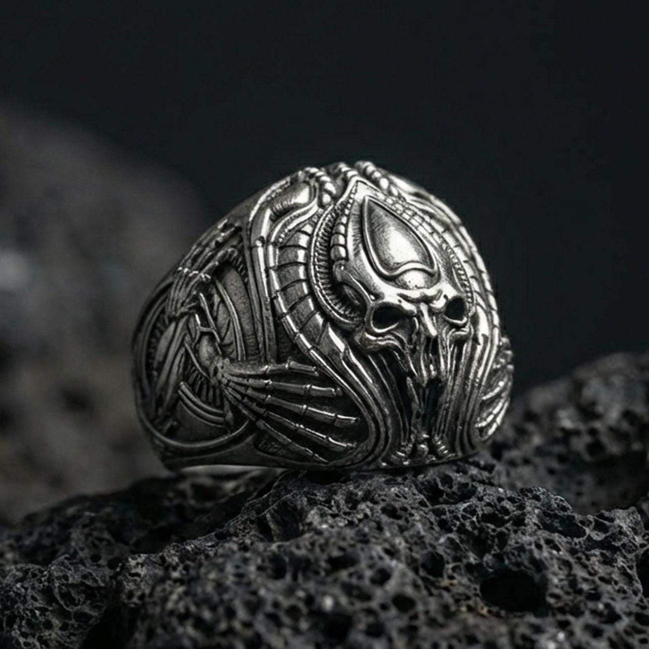 Oxidized biomechanical alien skull ring on black volcanic stone, sci-fi gothic signet, detailed xenomorph-style relief