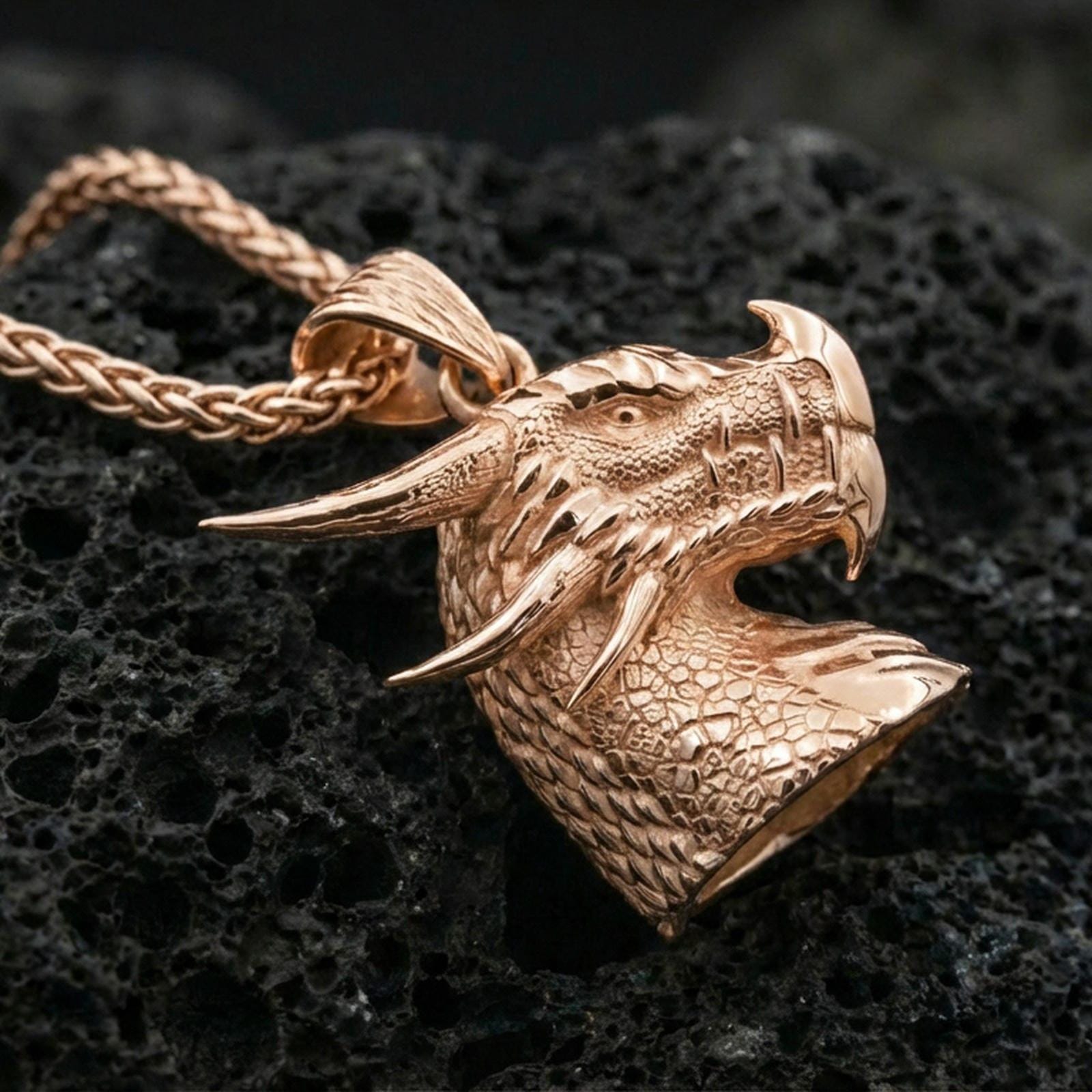 Rose gold plated dragon head pendant on matte volcanic stone, intricate reptile scales and curved horns, crisp macro focus