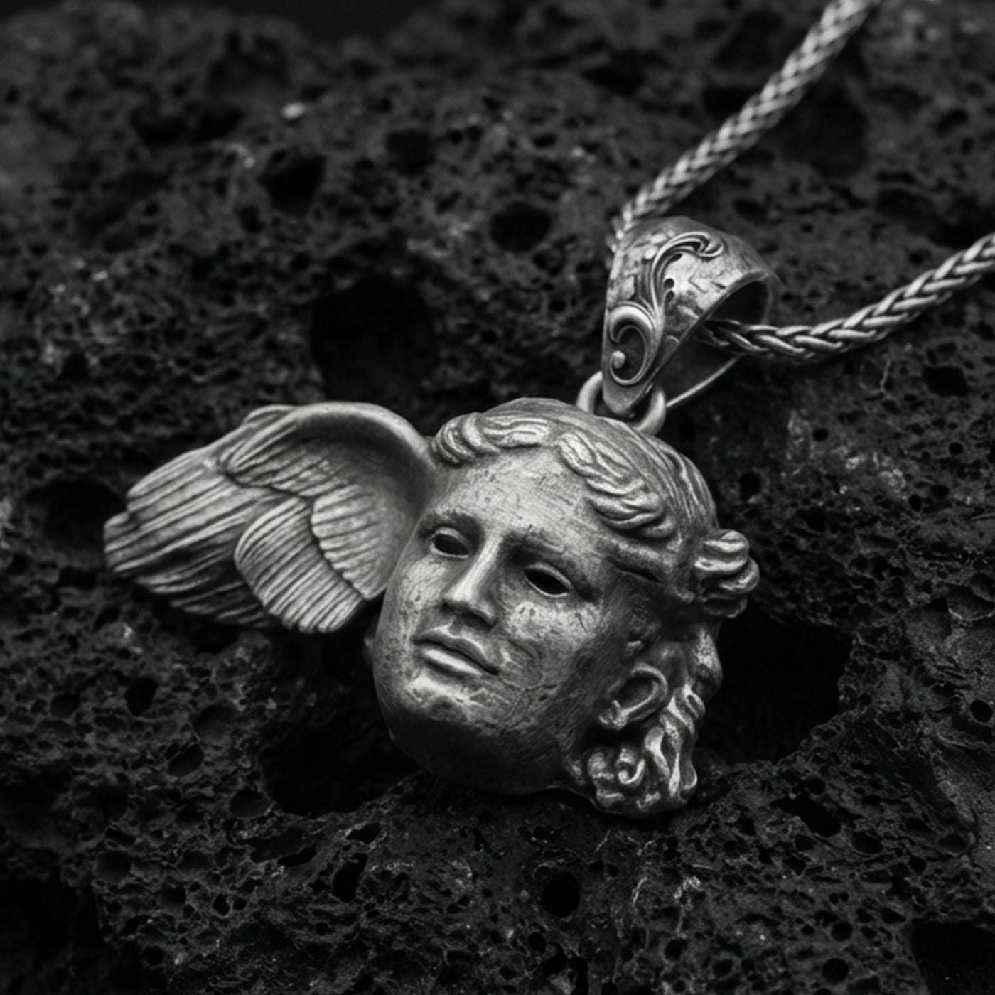 Oxidized sterling silver Hypnos pendant on textured volcanic rock, serene Greek god face with wing detail, macro studio shot