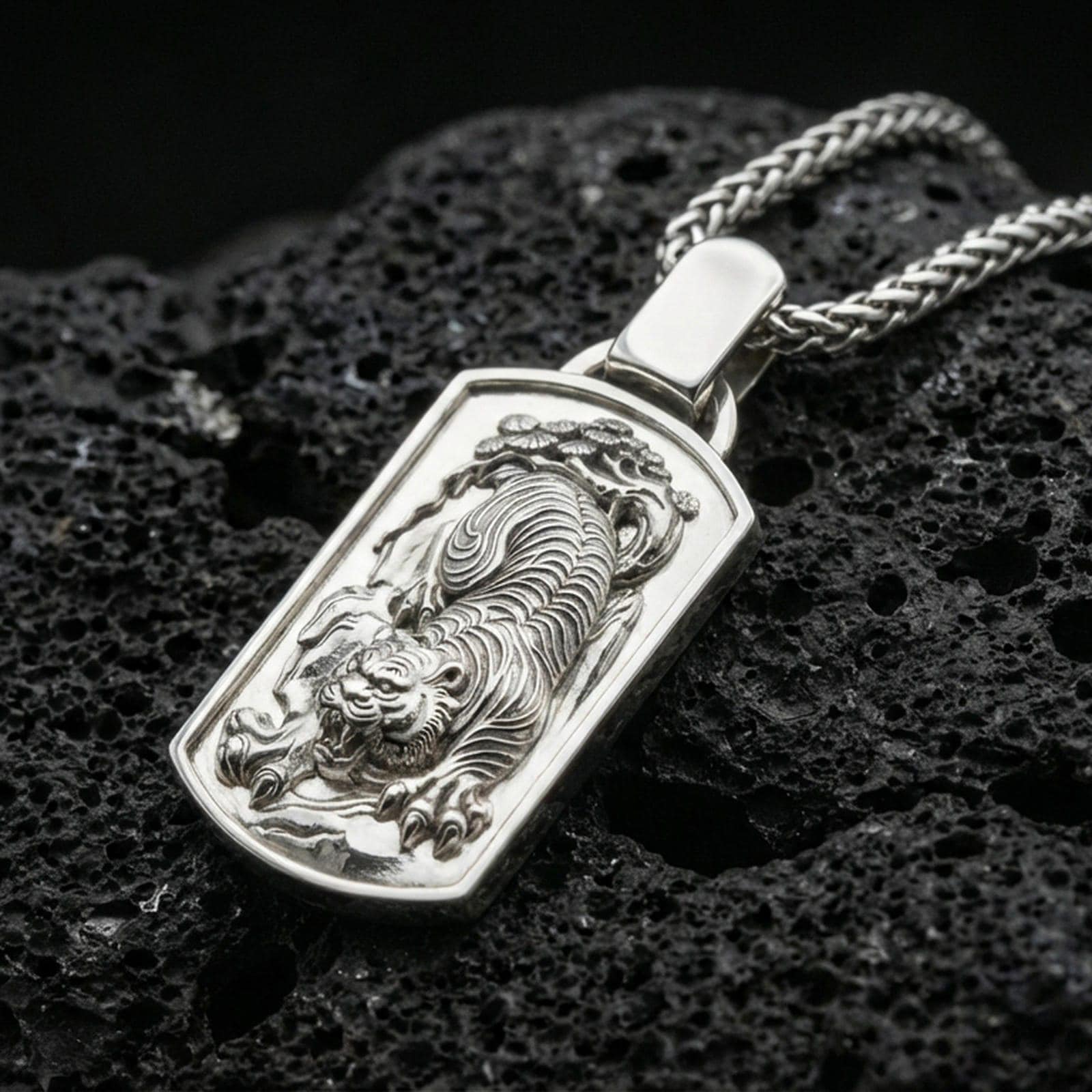 Polished silver zodiac tiger necklace pendant on dark volcanic stone, crisp engraved stripes and claw details, premium close-up composition