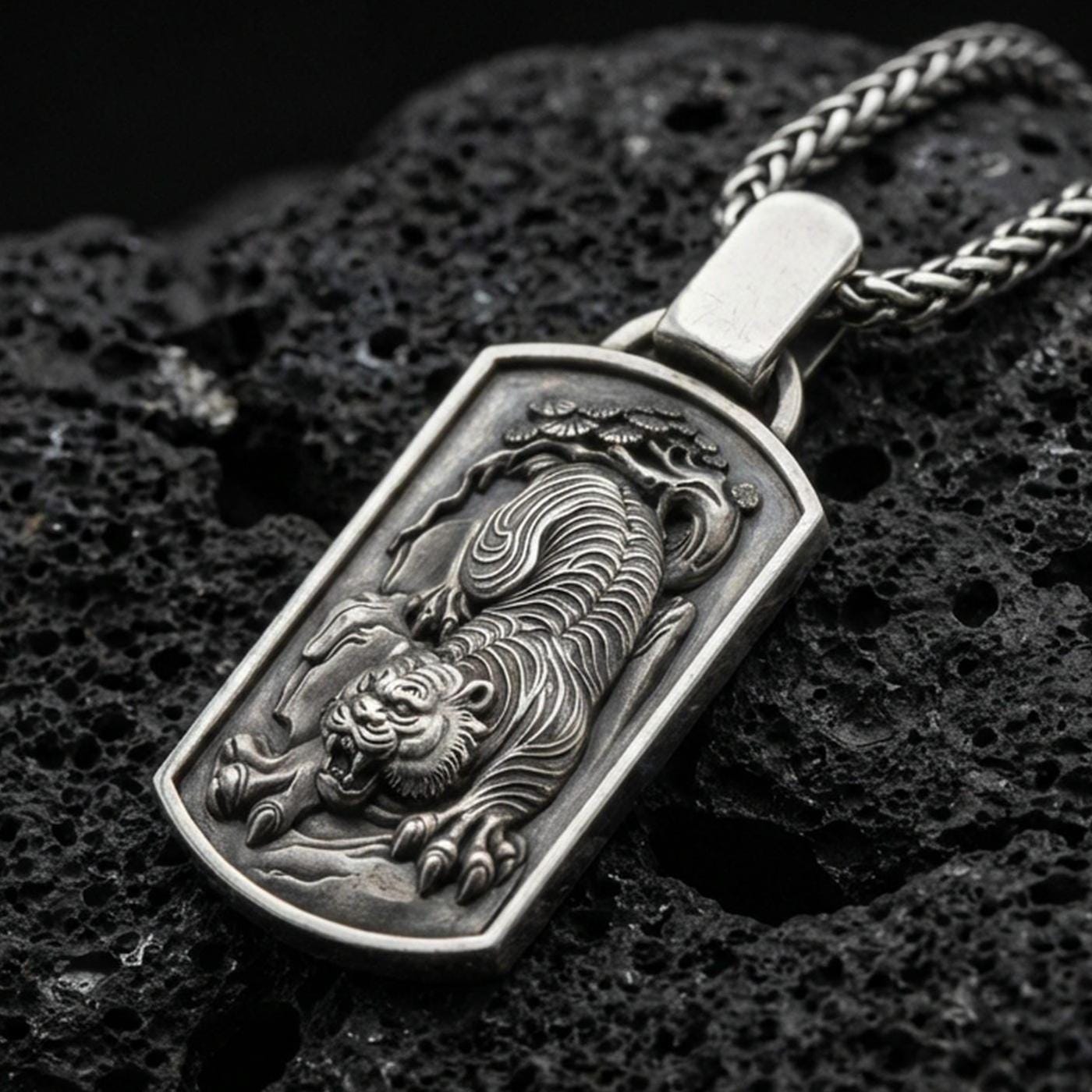 Oxidized sterling silver Chinese tiger pendant on textured volcanic rock, roaring tiger relief in rectangular tag frame, macro studio shot